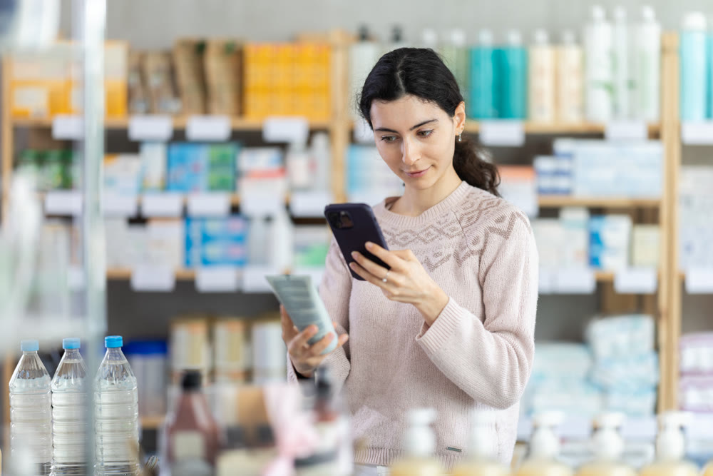 Girl in autumn clothes scans code on package of cream to check expiration date