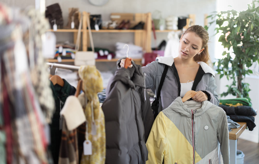 Female shopper carefully selects a fashionable jacket in clothing boutique.
