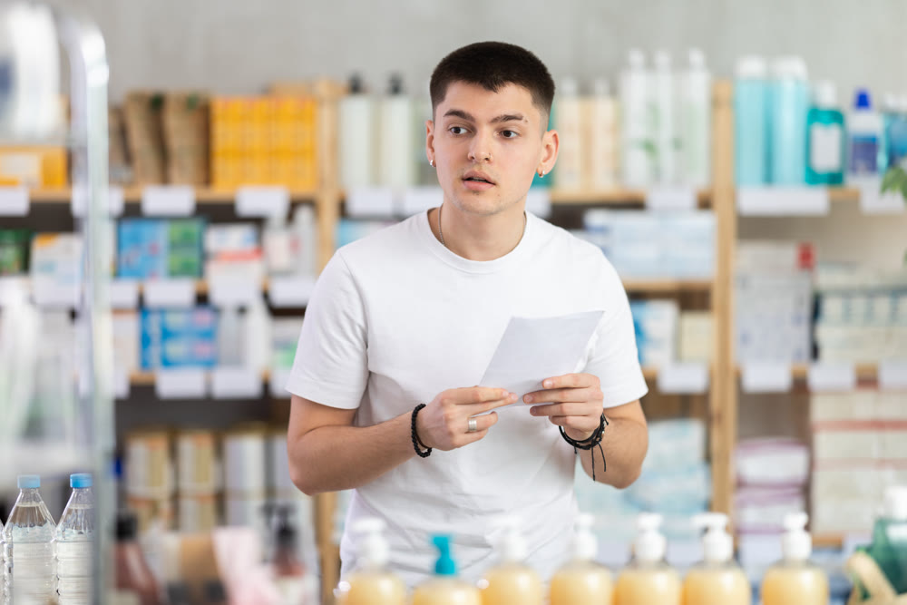 Portrait of young guy with prescription in hand looking for something in drugstore