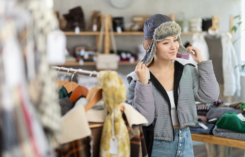 Young woman try on fur hat in store and carefully examines her reflection in mirror