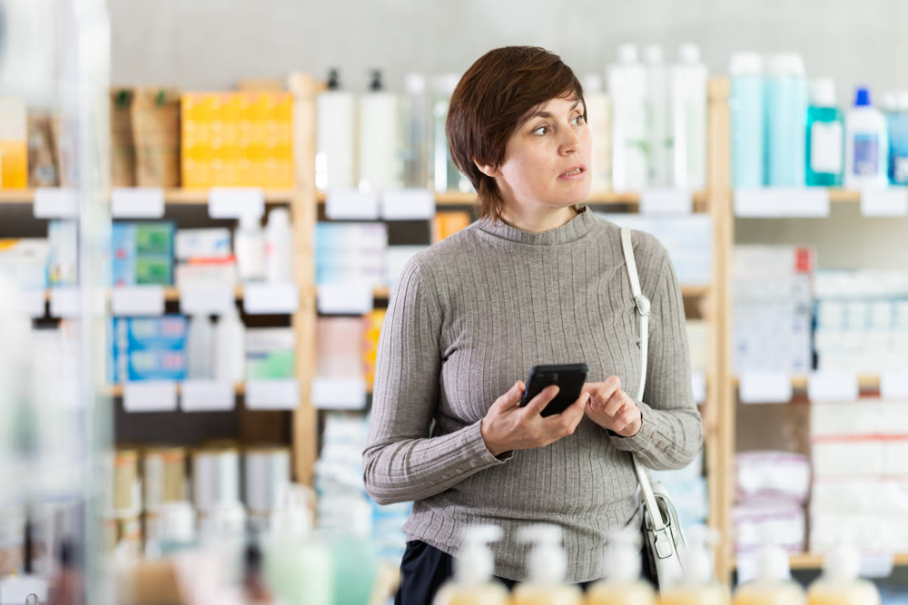 Woman checking list of needed items on phone while shopping at drugstore