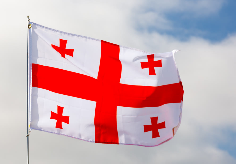 Against background of cloudy sky,white-red flag of Georgia flutters on flagpole