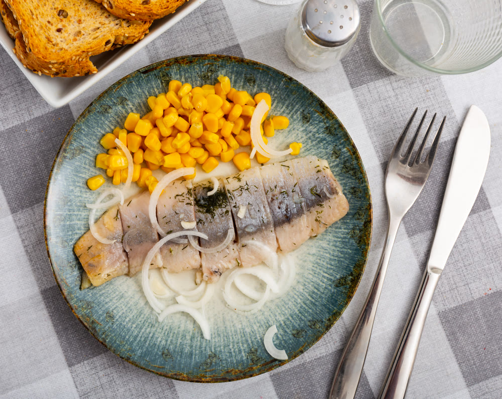 Sliced pickled herring fillet with corn and onions on plate