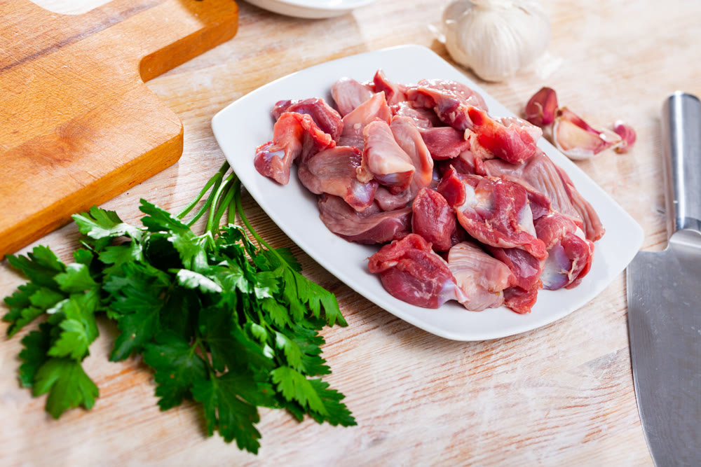 Raw chicken gizzards before cooking on table with greens