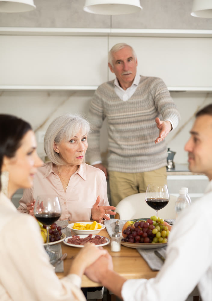 Concerned parents watching adult son communicating with girlfriend at dinner table
