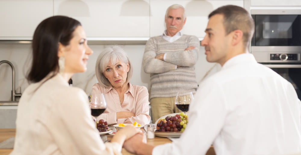 Concerned parents watching adult son communicating with girlfriend at dinner table