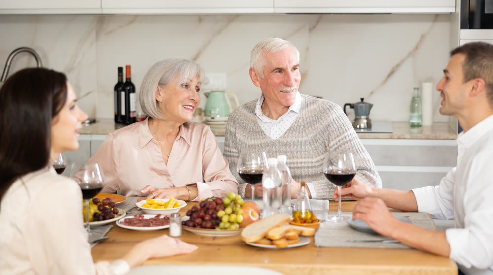 Mature married couple are sitting at table, enjoying food and wine with middle-aged guests.