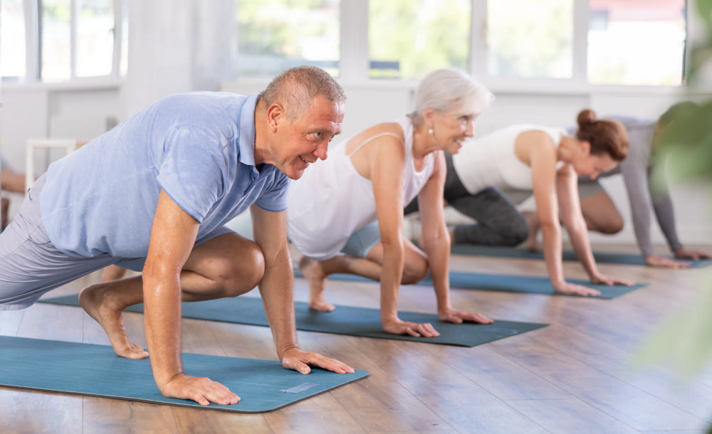 Diligent women and men doing body stretching before yoga class in a fitness studio