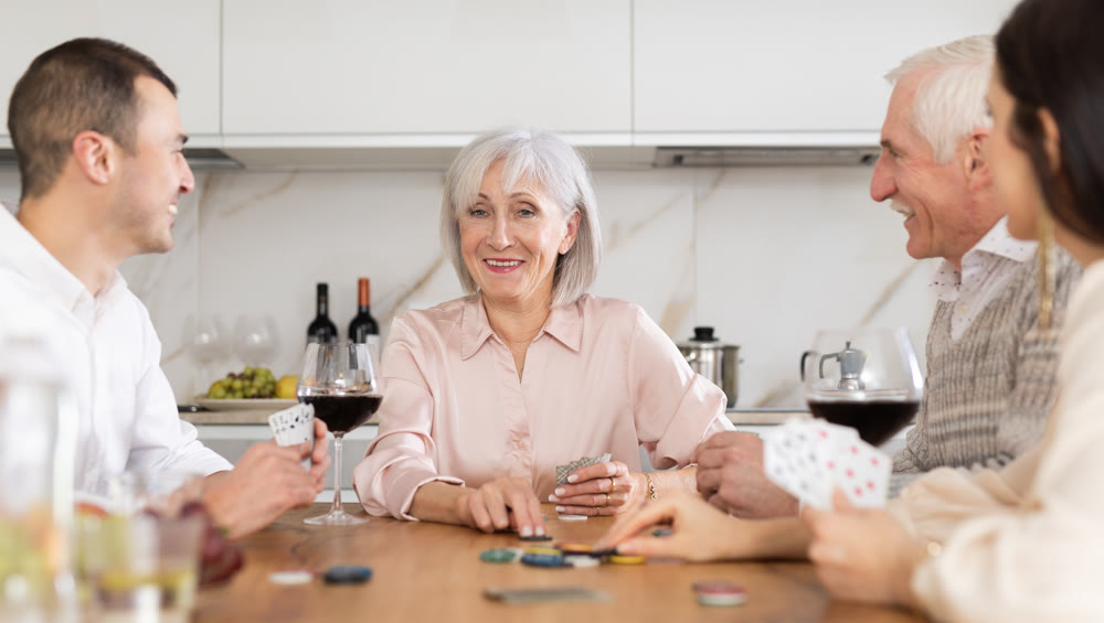 Joyful senior parents and young couple sitting around table playing poker