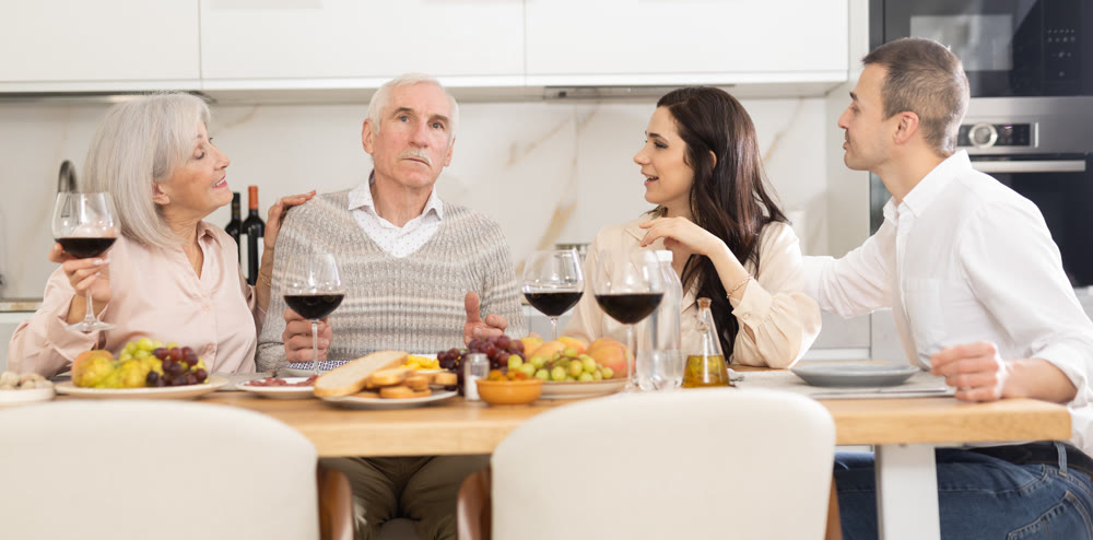 Mature married couple are sitting at table, enjoying food and wine with middle-aged guests.