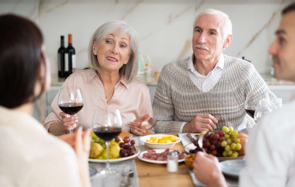 Mature married couple are sitting at table, enjoying food and wine with middle-aged guests.