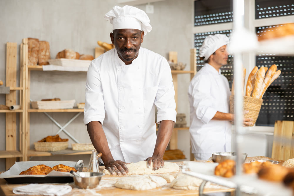 Two male bakers knead dough and put baked goods