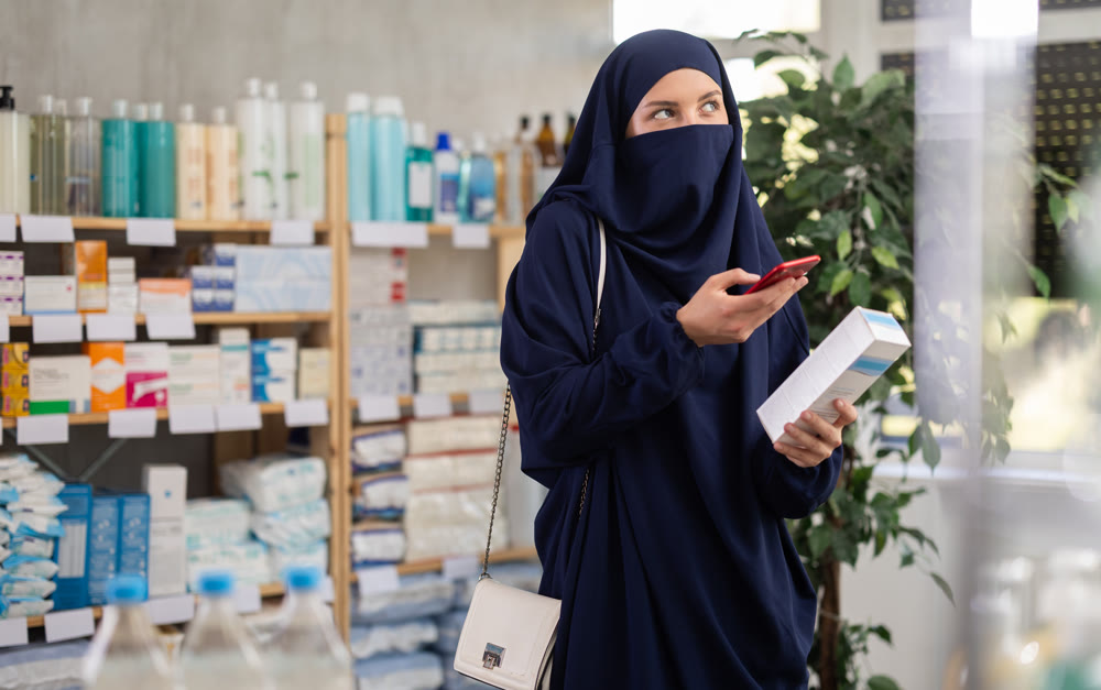 Young woman in hijab scanning qr code of cream