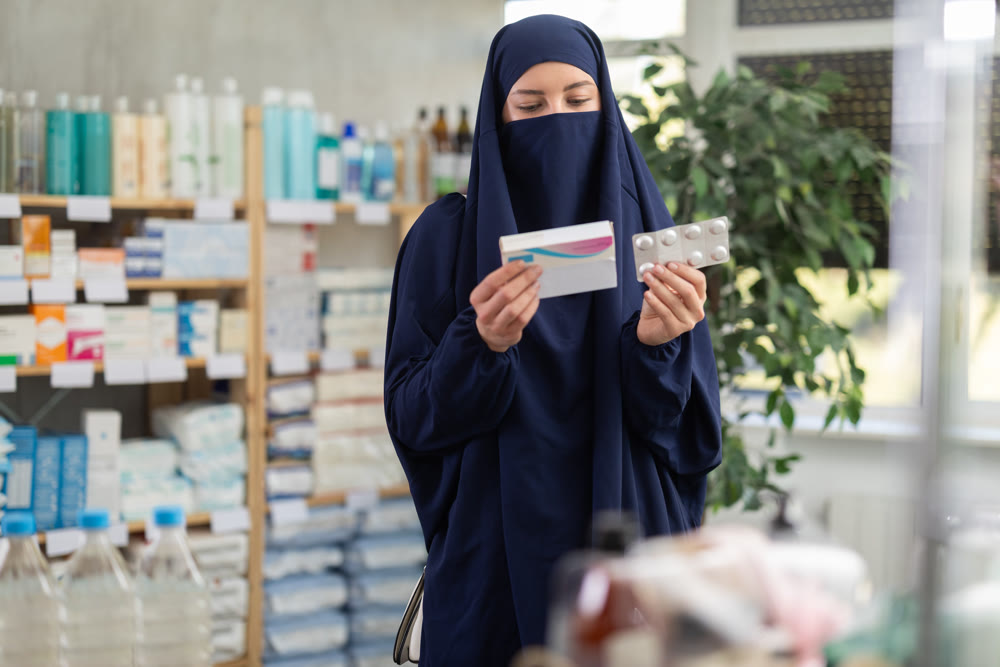 Young Muslim woman customer choosing pills in box in drugstore
