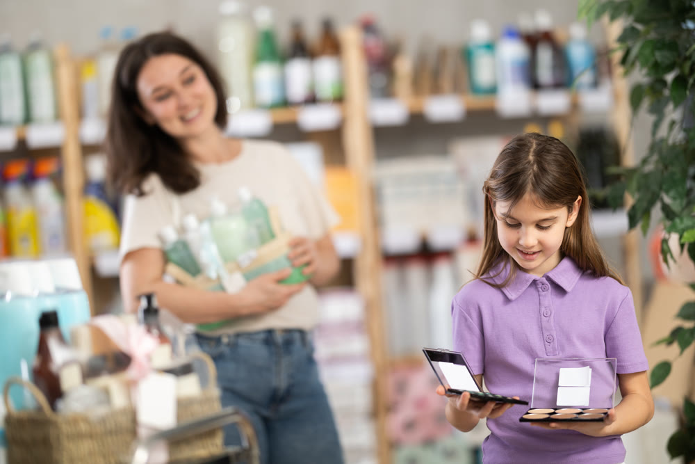 Little girl longingly looks at eye shadow pallet in shop and dreams of makeup like adult lady