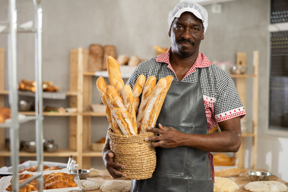 Successful African baker holding freshly baked baguettes