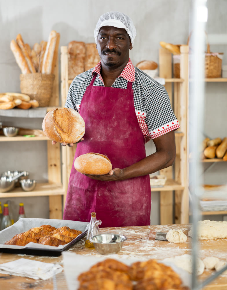 Smiling black baker offering crusty bread in bakery