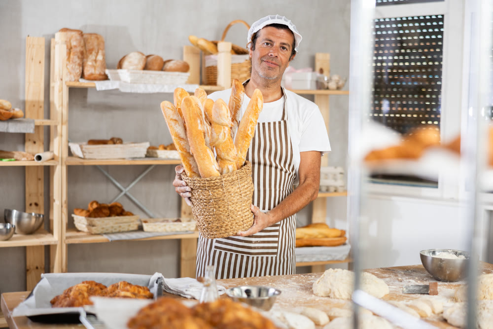 Caucasian male cook-baker worker with basket of baguettes, shows many products