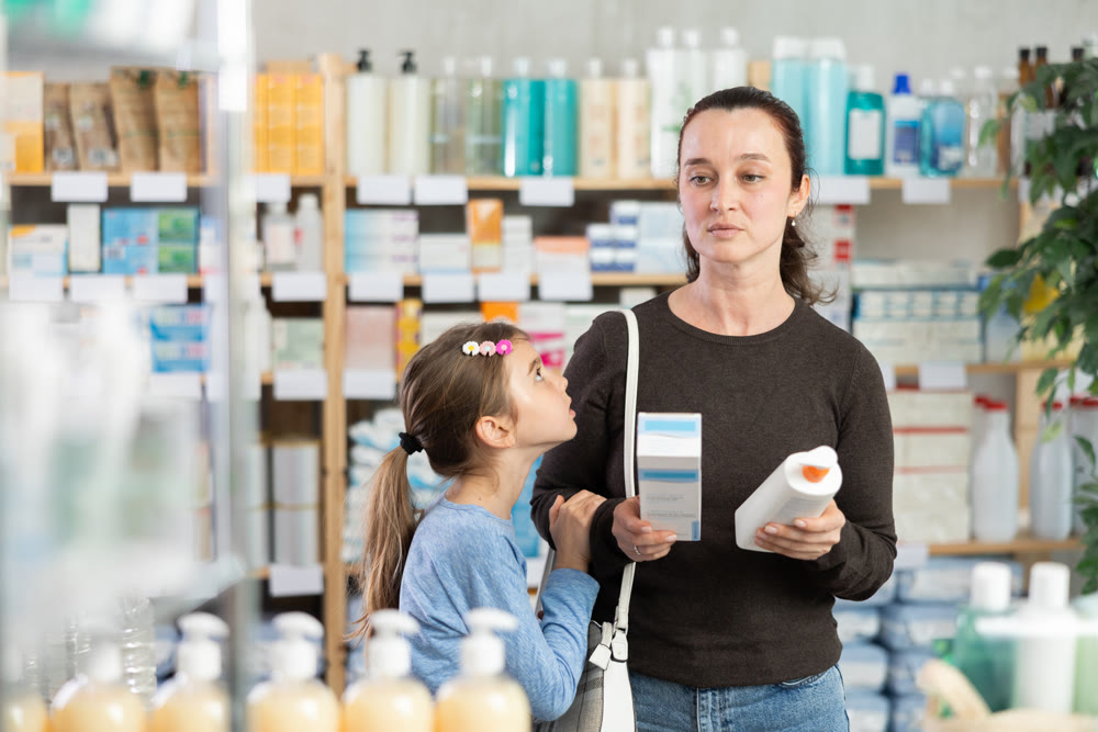 Woman with schoolgirl daughter are busy choosing cream at pharmacy