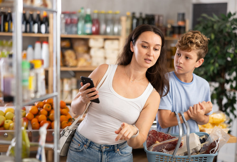 Adult woman with phone and son choosing groceries in store
