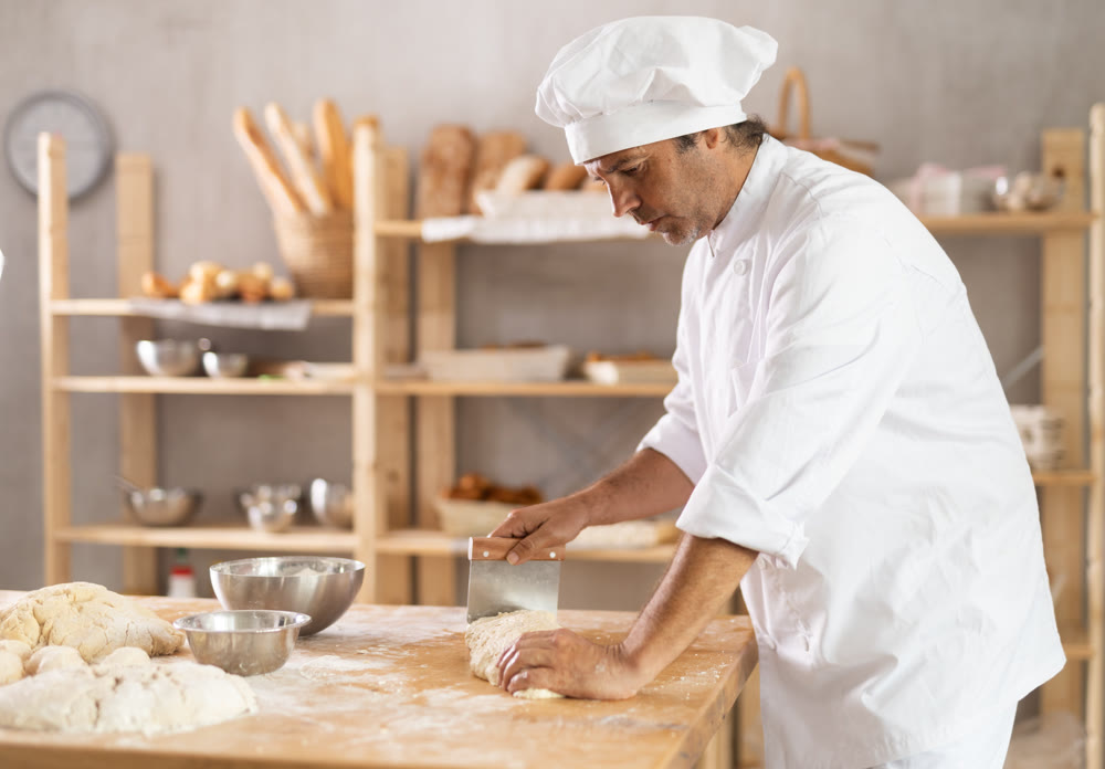 Professional male baker uses knife to cut raw dough to make croissants or buns