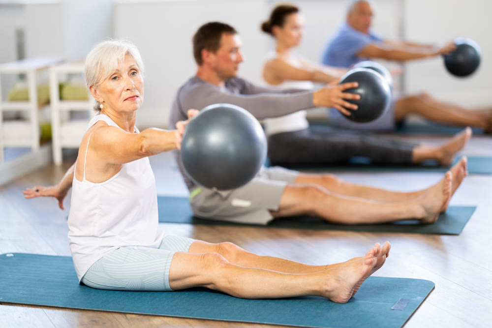Group of mature people in sportswear exercising Pilates with soft balls while sitting on mats in fitness studio