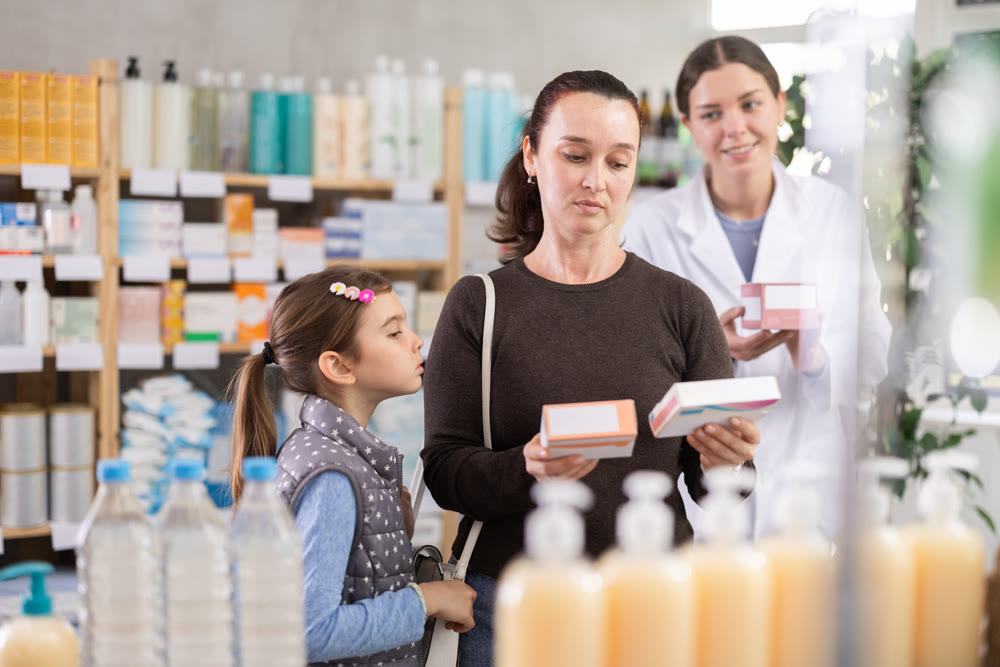 Middle-aged woman with daughter choosing pills in drugstore