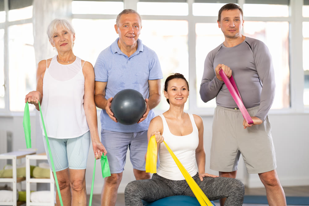 Coach and elderly visitors of fitness course smile happily after training