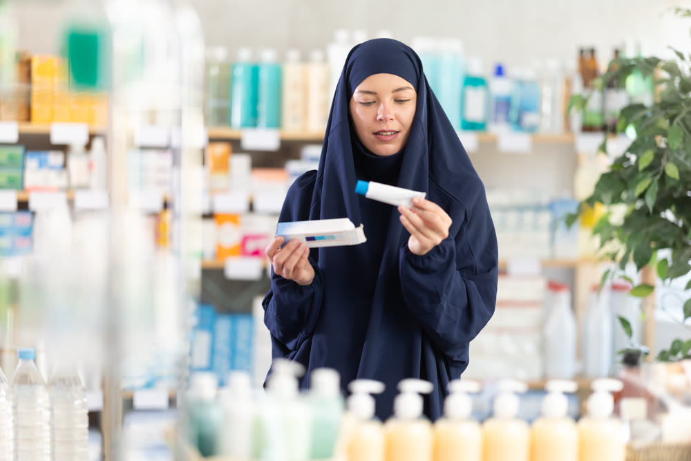 Young Muslim woman choosing regenerating ointment in drugstore
