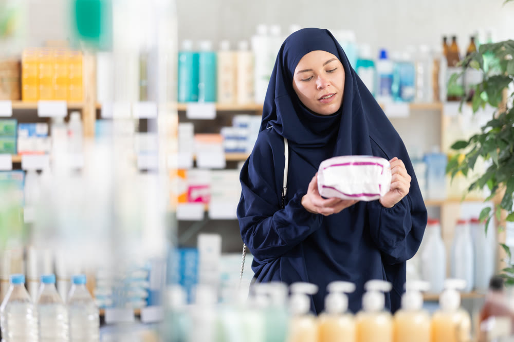 Young woman in hijab chooses feminine pads at pharmacy