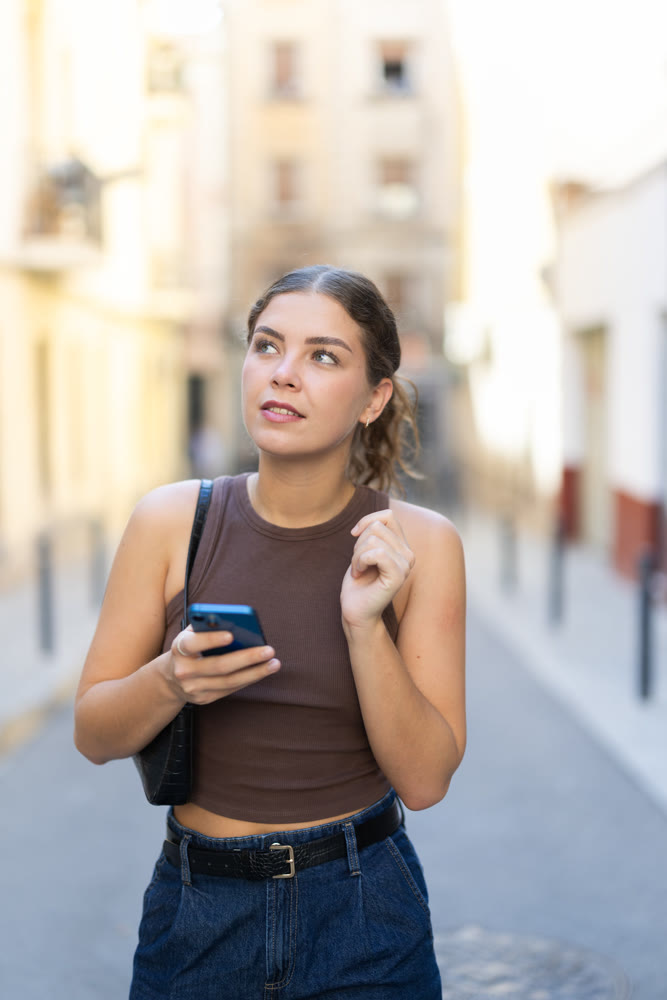 Young woman looking at smartphone while walking along street