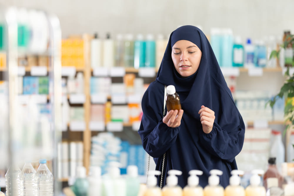 Young Muslim woman customer choosing syrup in drugstore