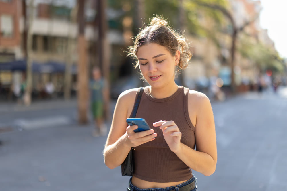 Young woman looking at smartphone while walking along street