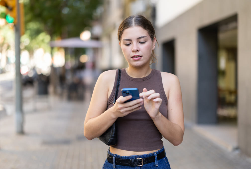 Young woman looking at smartphone while walking along street