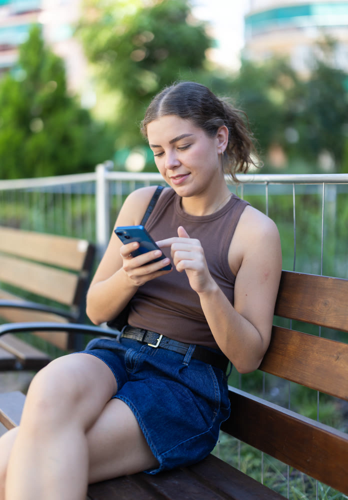 Woman scrolling smartphone while sitting on bench