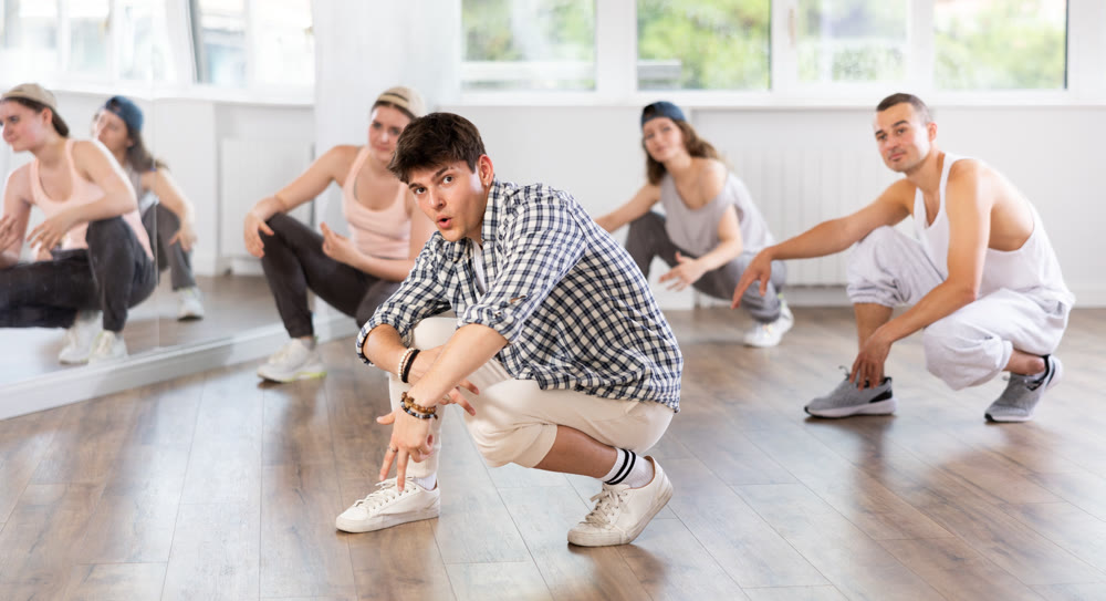 Young guy performing sitting pose of breakdance in training hall