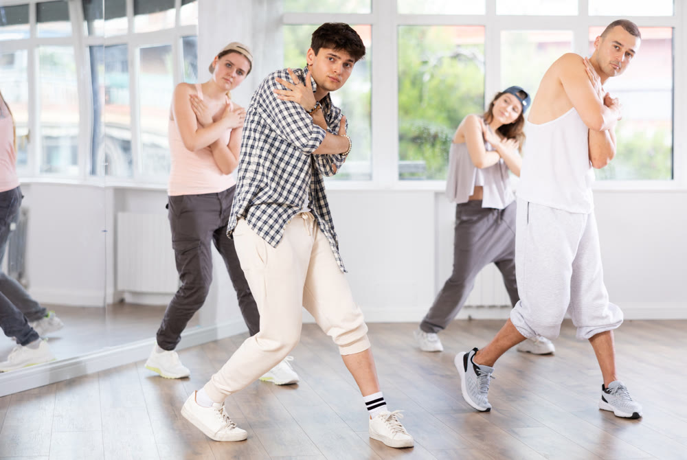 Young man standing performs basic hip hop movements in front of group of students