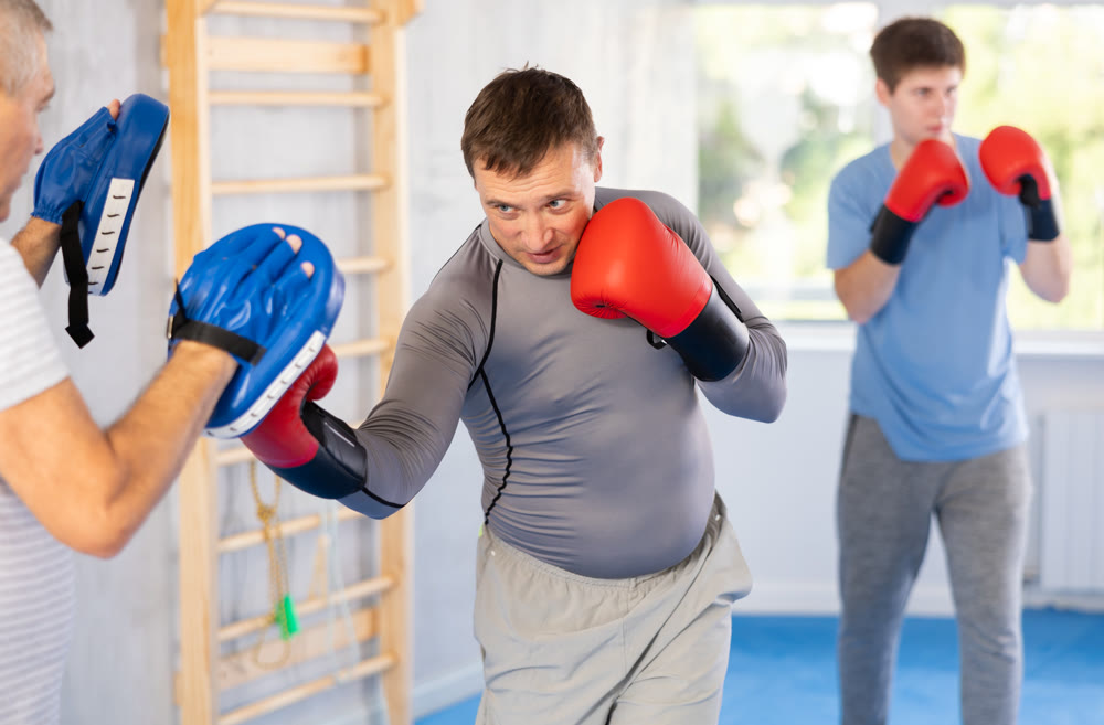 Man in boxing gloves practicing punches on mitts during self-defense course