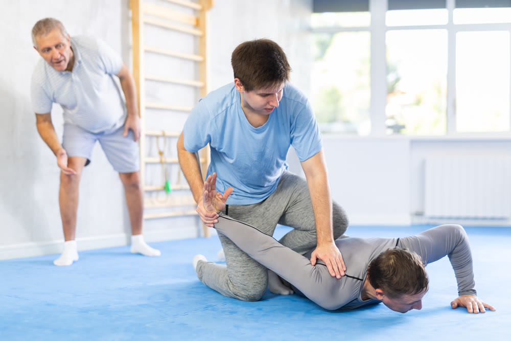 Two athlete men of different age in sportswear practicing self-defense sparring in hall
