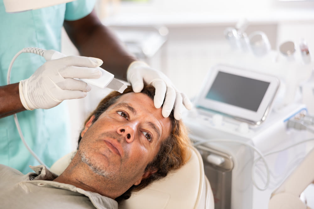 African male doctor uses scriber beauty machine nozzle for gentle skin peeling for man client