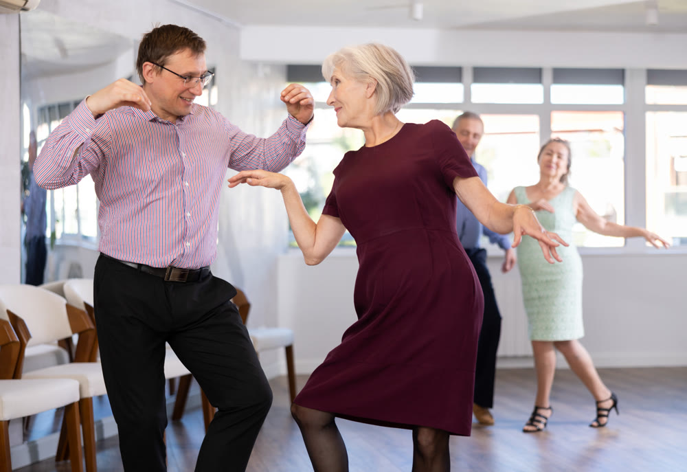 Group of adult active people practicing vogue dancing movements while training twist or rock and roll dance in dance hall
