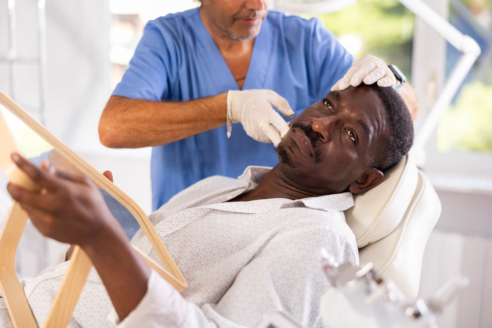 Male cosmetologist examines face of African man patient and consult on possibility of rejuvenation