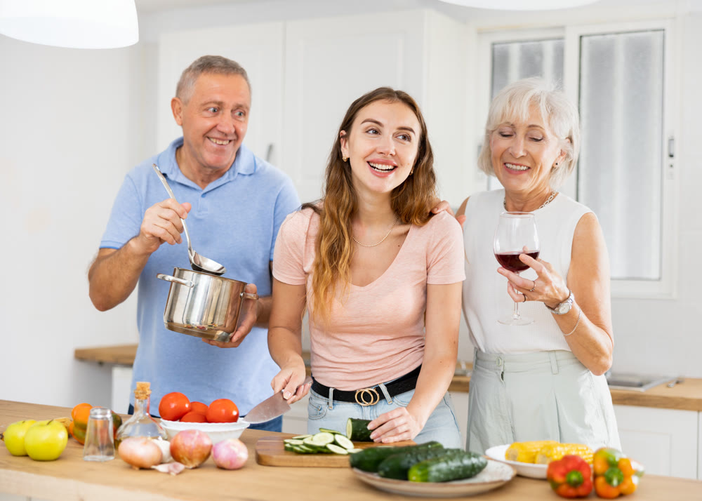 Senior couple spending time together with their adult daughter, cooking delicious meals for dinner