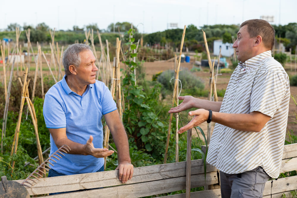 Two male farmers talking outside next to wooden fence on background with farm
