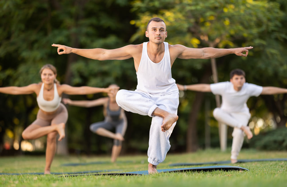Yoga lesson visitors with coach perform Garudasana in park