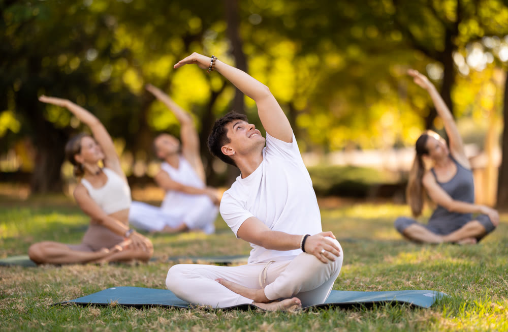 Guy performing stretches in lotus position during group yoga outdoors