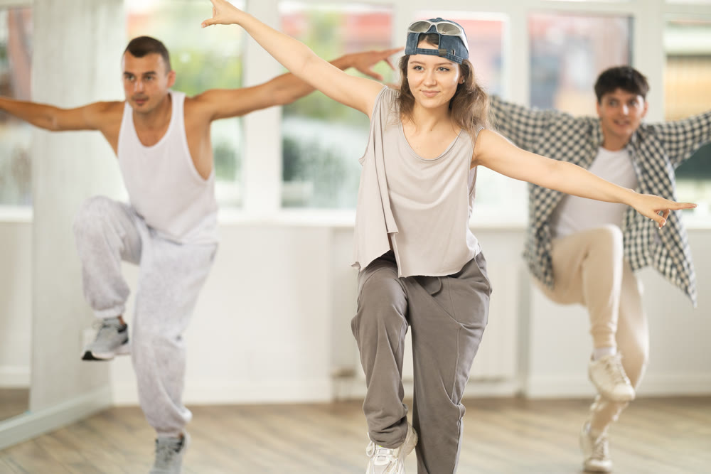 Young girl standing performs basic hip hop movements in front of group of students