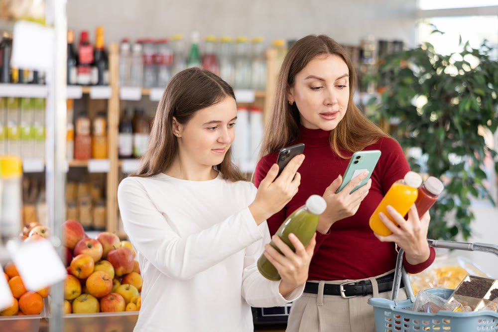 Teenage girl and her mother scanning QR on bottle of smoothie in supermarket
