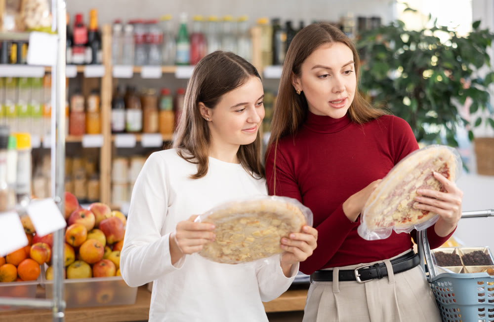 Teenage girl and her mother choosing pizza in grocery store