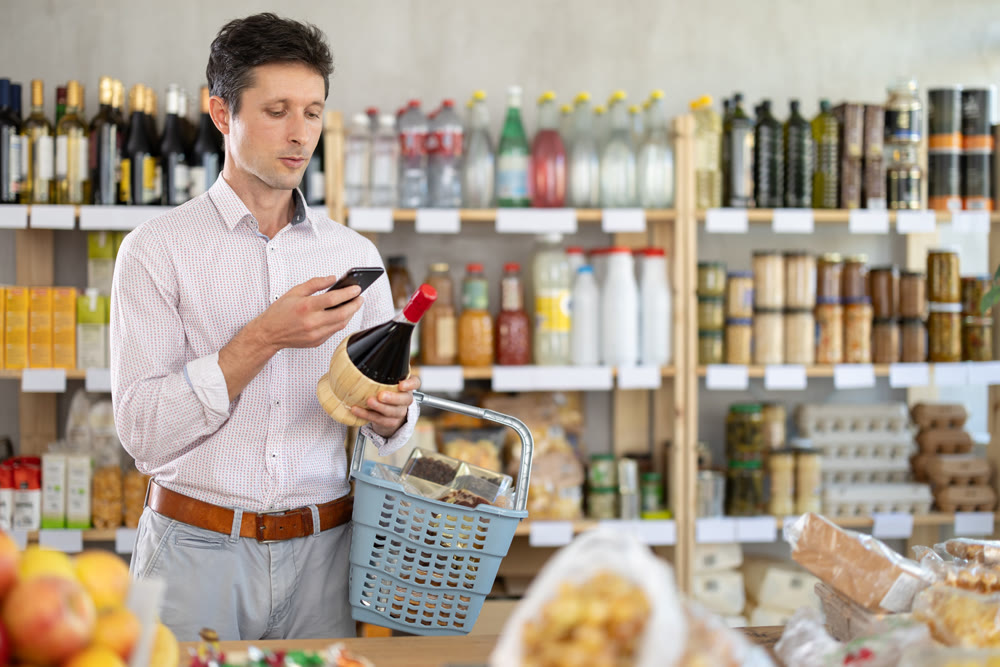 Man in light shirt scan QR code and take reading wine using phone camera in shop